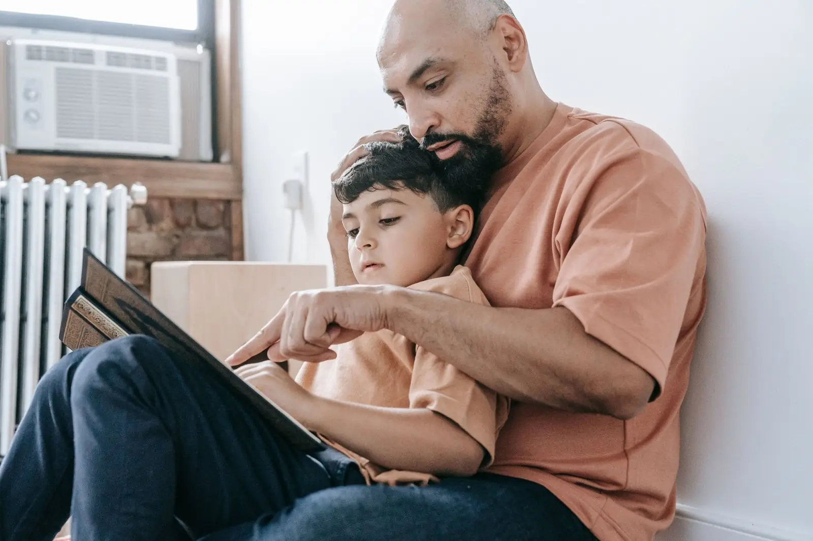 A father sitting on the floor at home, reading with his young son on his lap