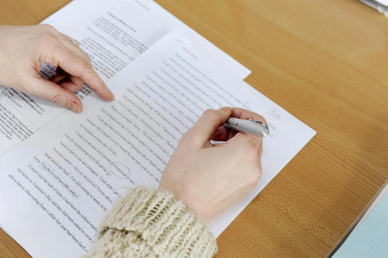 Person marking up a typed draft with a pen while checking an earlier version