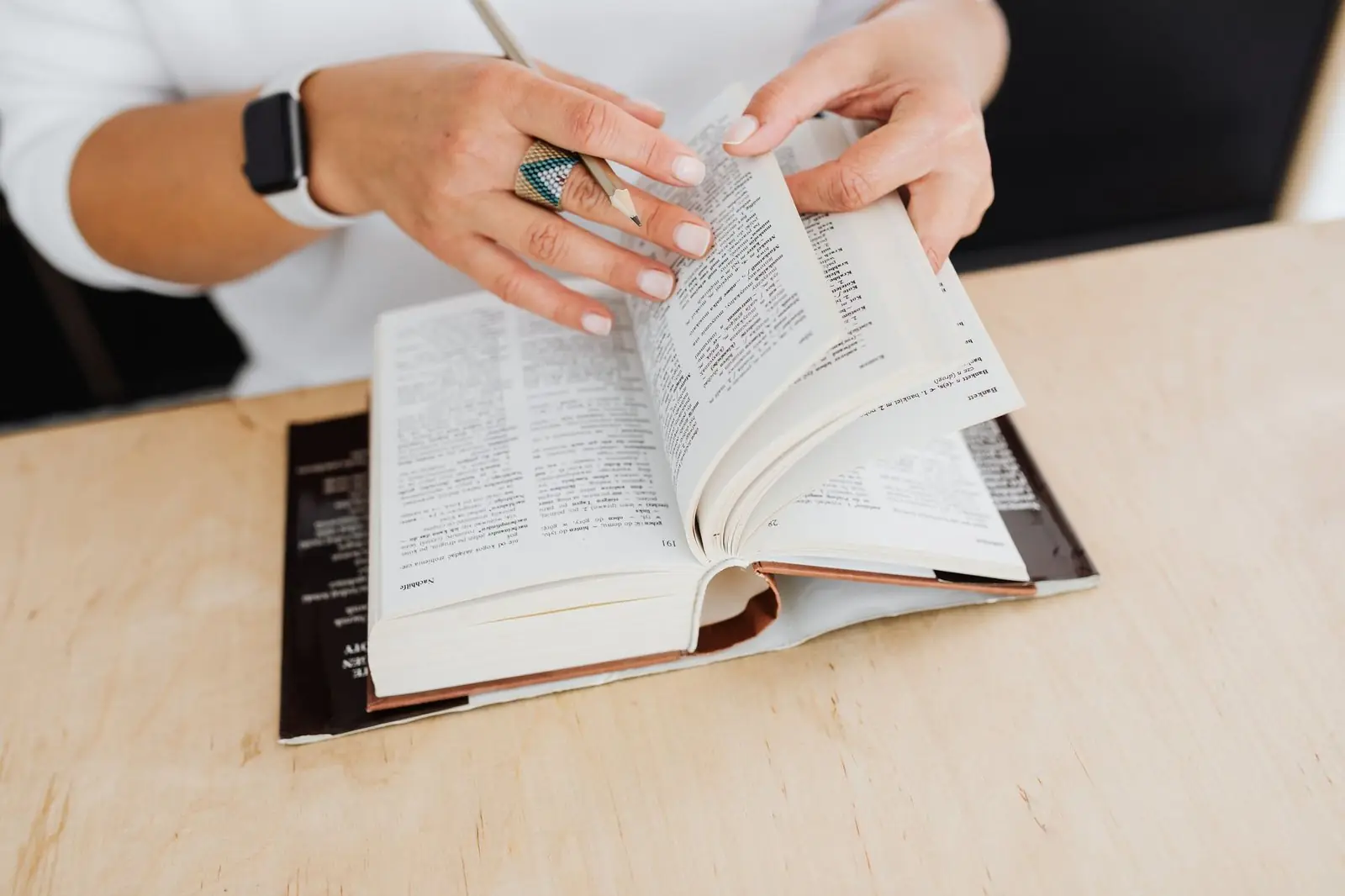 Hands turning the pages of a thick dictionary