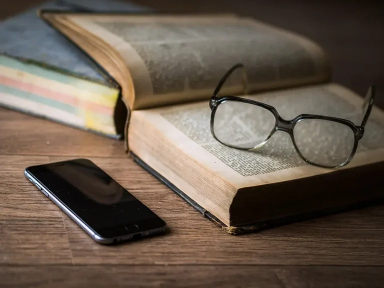 Reading glasses on an old open book beside a phone
