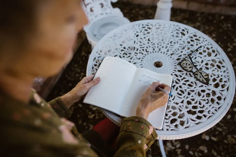 Older woman writing in a notebook at a garden table