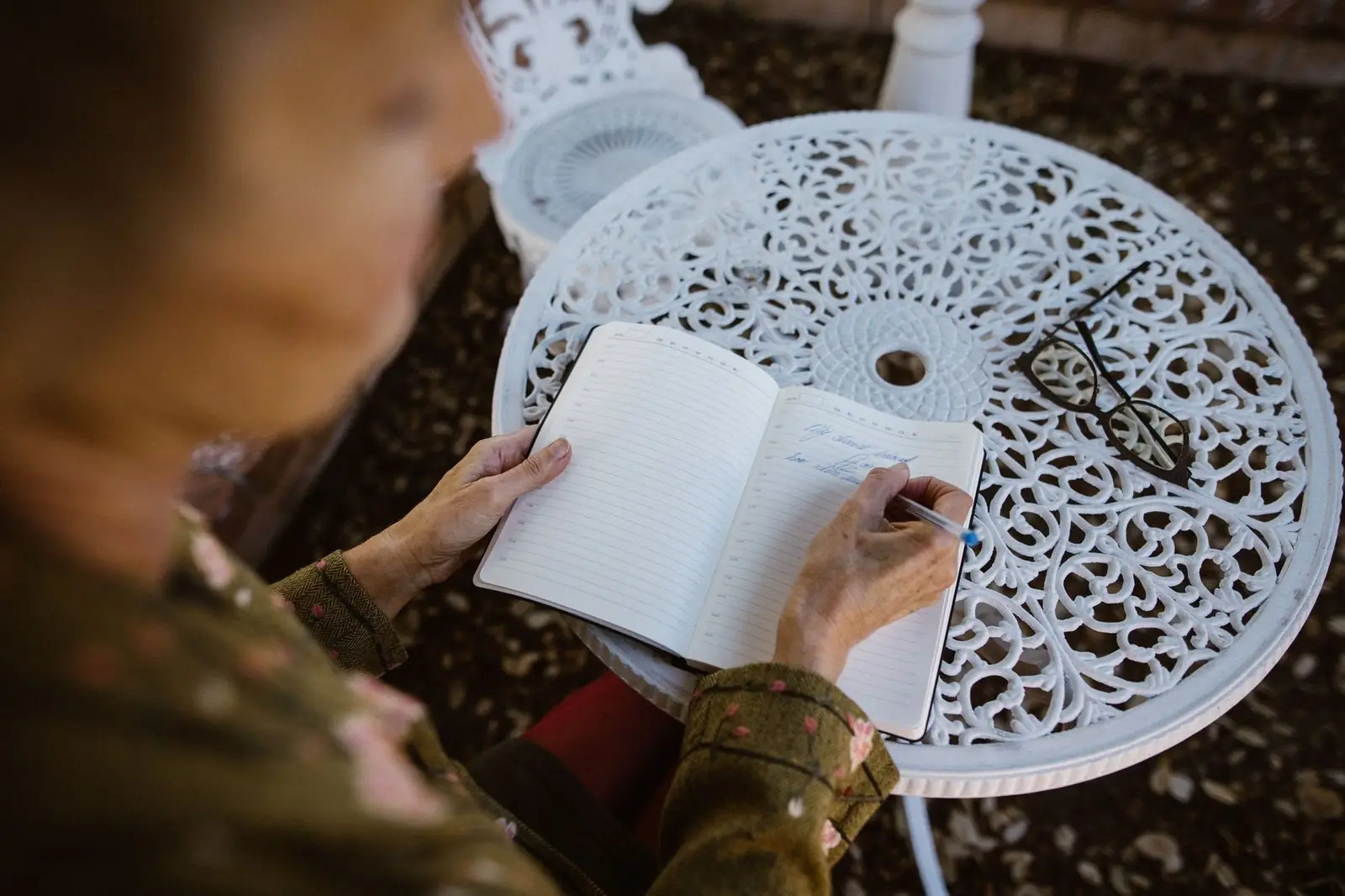 Older woman writing in a notebook at a garden table